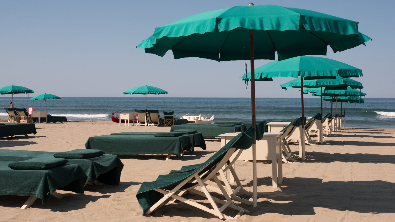 Ombrelloni verdi, lettini e sedie da regista davanti al mare